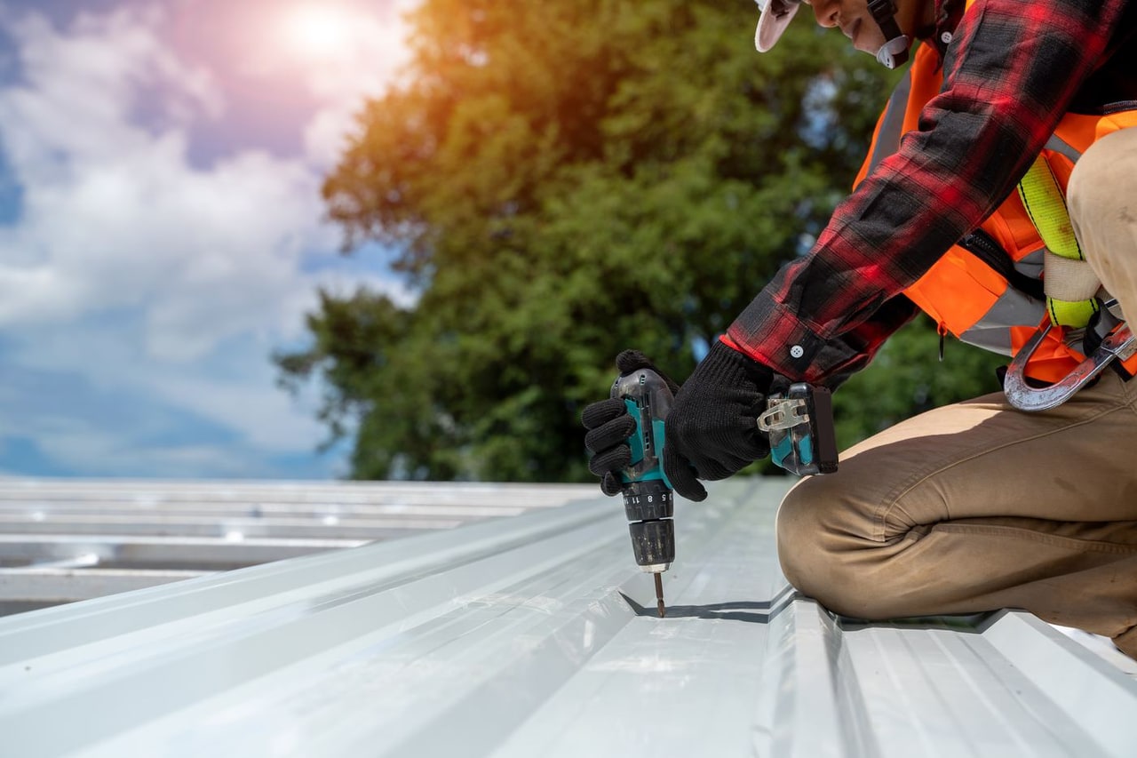 Roofer fastening a metal roof panel with a cordless drill