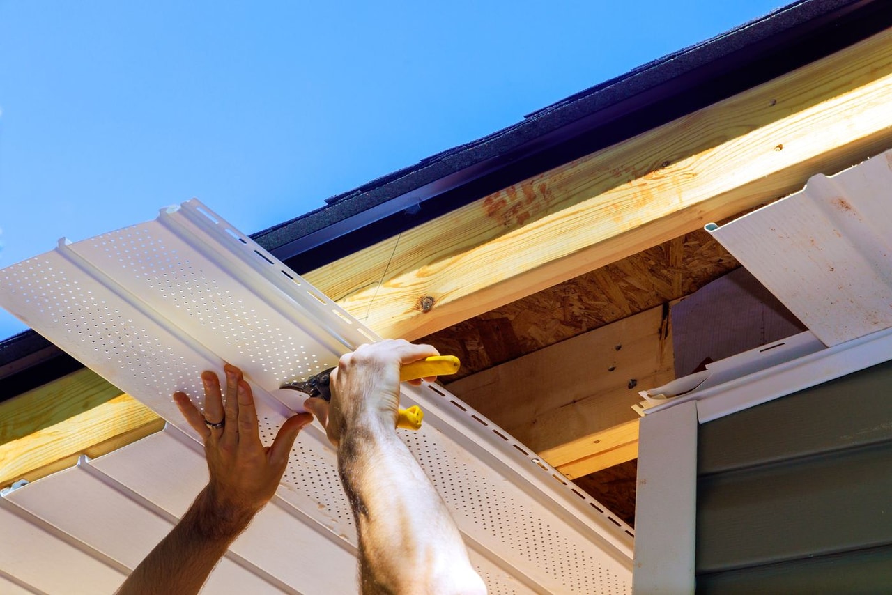 Worker fitting a perforated soffit panel under a roof eave